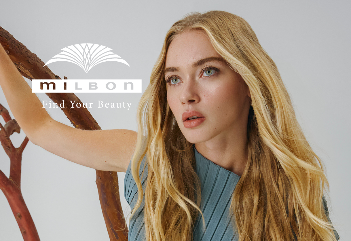 Kvinne med langt, bølgete blondt hår som ser til siden foran lysegrå bakgrunn, med rødlige tregreiner bak og MILBON-logoen med teksten ‘Find Your Beauty’ til venstre i bildet