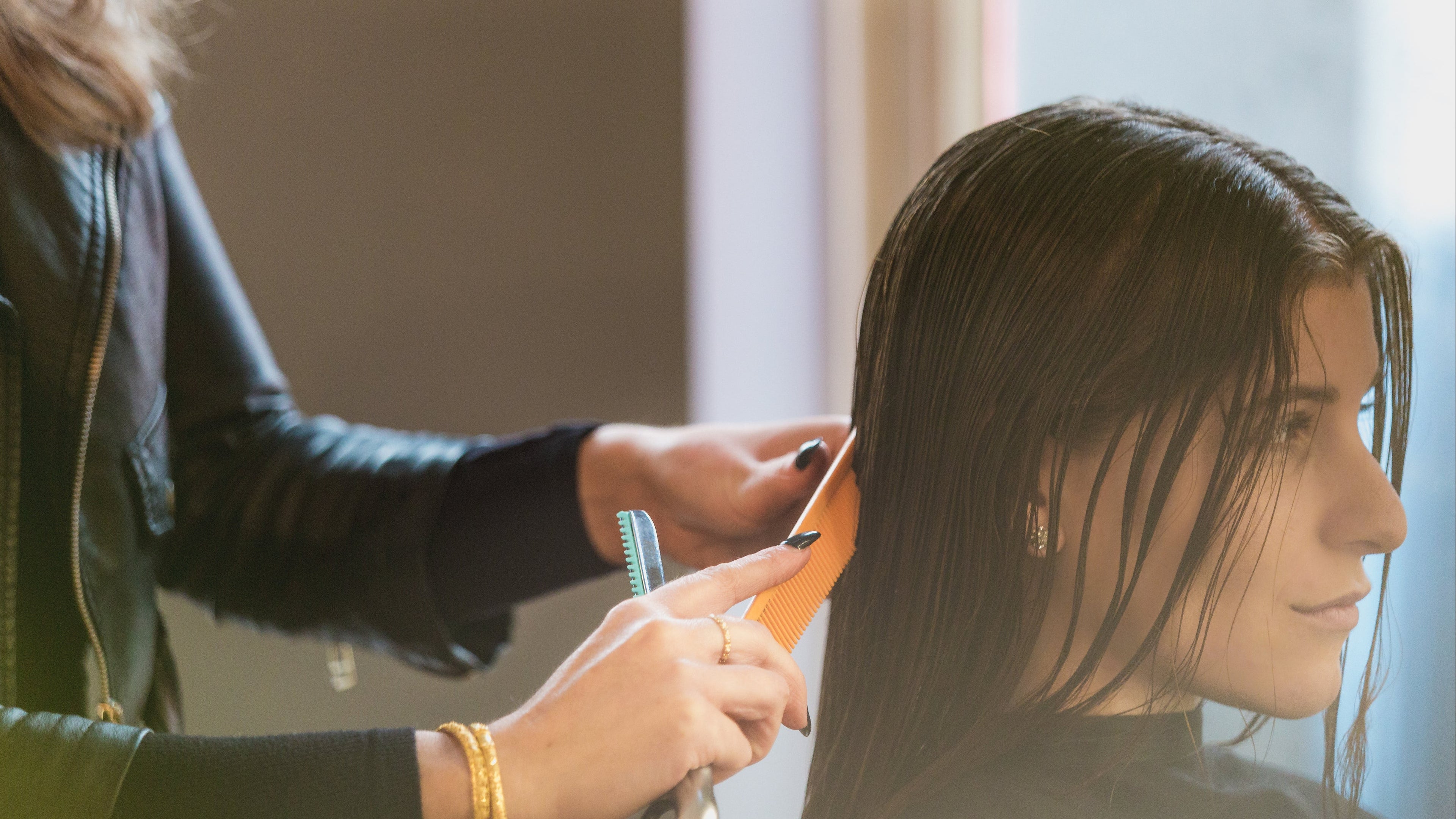 Frisør som klipper vått, mørkt hår på kvinne ved hjelp av kam og saks i salong.