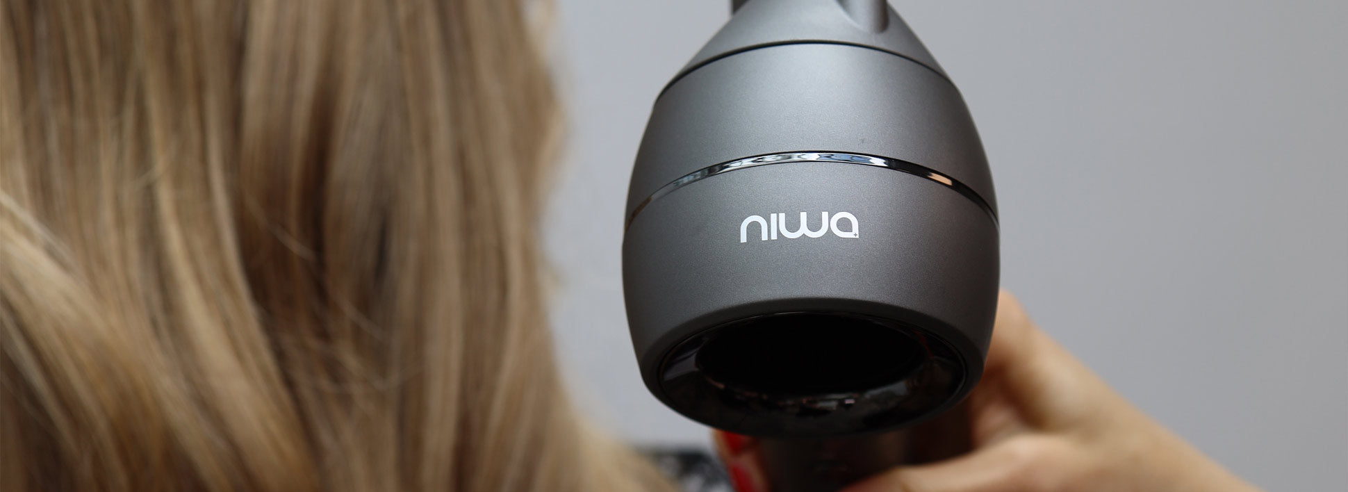 Nærbilde av grå NIWA hårføner rettet mot langt blondt hår.